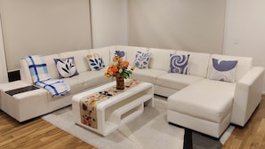 Uma sala de estar moderna com um sofá branco, uma mesa de centro estampada e almofadas decorativas.