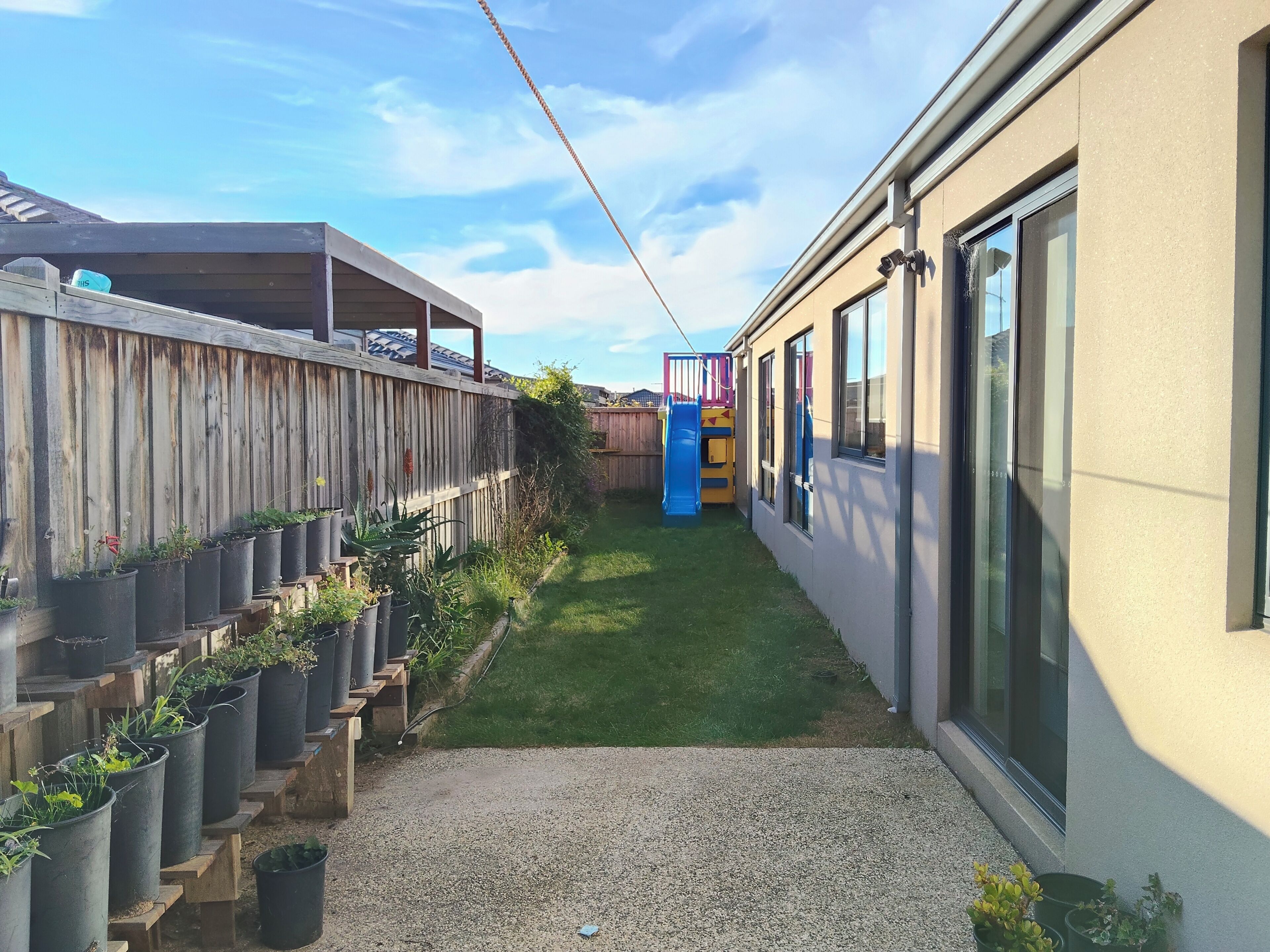 A residential backyard with a wooden fence, a small play structure, and potted plants.
