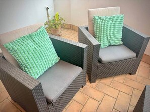 Two wicker chairs with grey cushions and green patterned pillows, placed on a tiled patio. - Gerona Luxury Apartments (Seville)