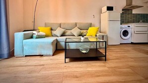 A living room with a sofa, coffee table, and a washing machine in the background. - Gerona Luxury Apartments (Seville)