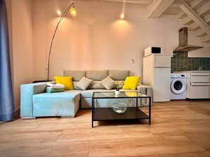 A living room with a sofa, coffee table, and a washing machine in the background. - Gerona Luxury Apartments (Seville)