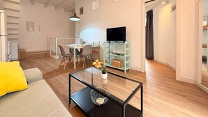 A modern living room with a sofa, coffee table, TV, dining area, and a staircase. - Gerona Luxury Apartments (Seville)