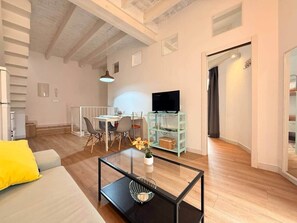 A modern living room with a sofa, coffee table, TV, dining area, and a staircase. - Gerona Luxury Apartments (Seville)