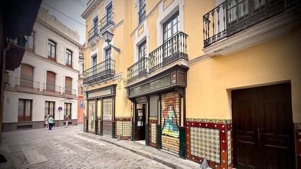 A cobblestone street with buildings featuring balconies and a shop with a closed shutter. - Gerona Luxury Apartments (Seville)