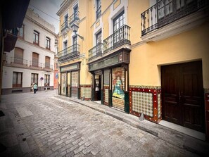 Una calle adoquinada con edificios que tienen balcones y una tienda con una persiana cerrada.
