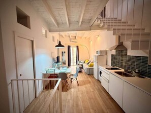 A modern kitchen with white cabinets, a dining area with a table and chairs, and a staircase leading to an upper level. - Gerona Luxury Apartments (Seville)