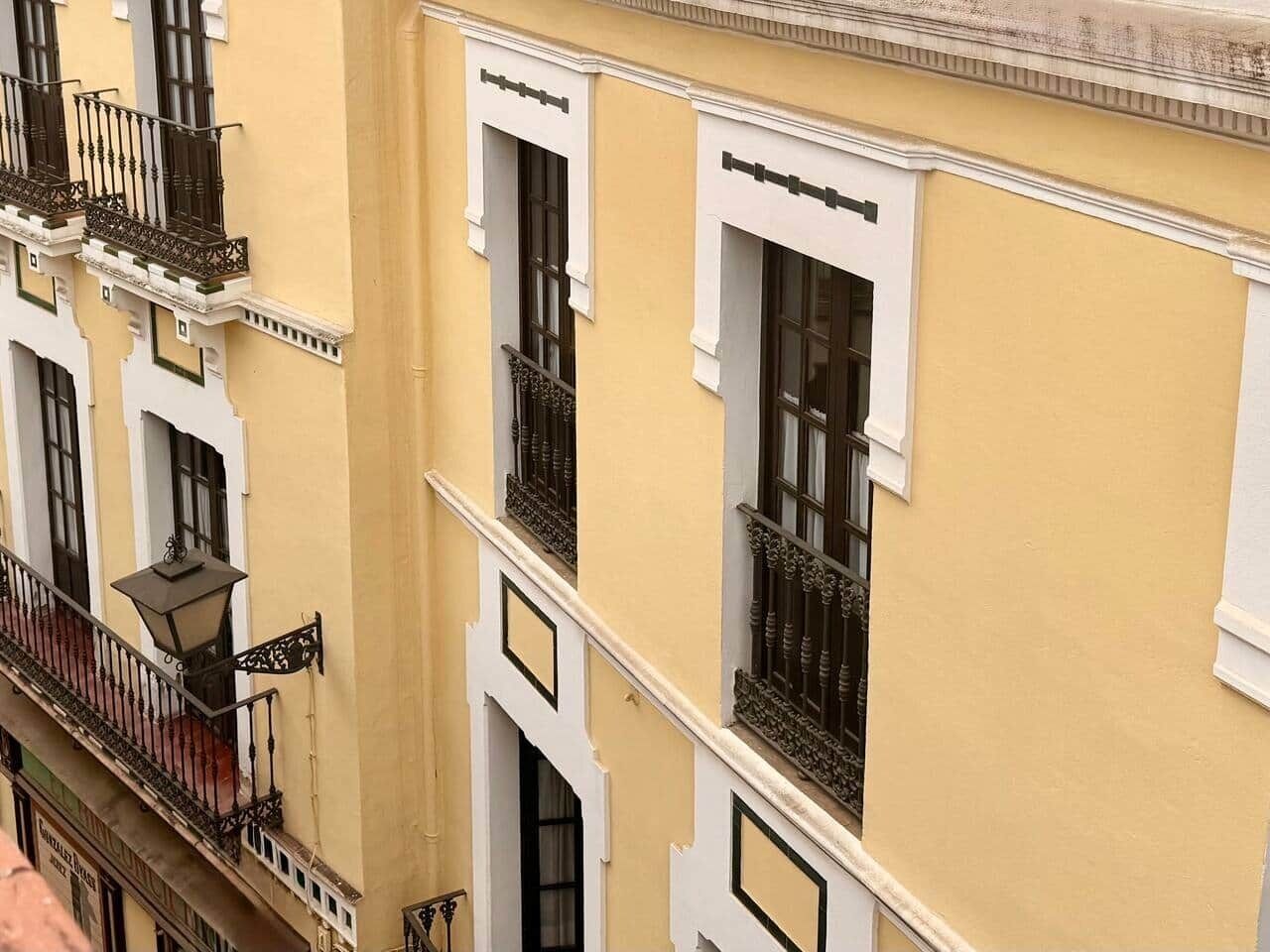 A multi-story building with balconies, white-framed windows, and a yellow facade.