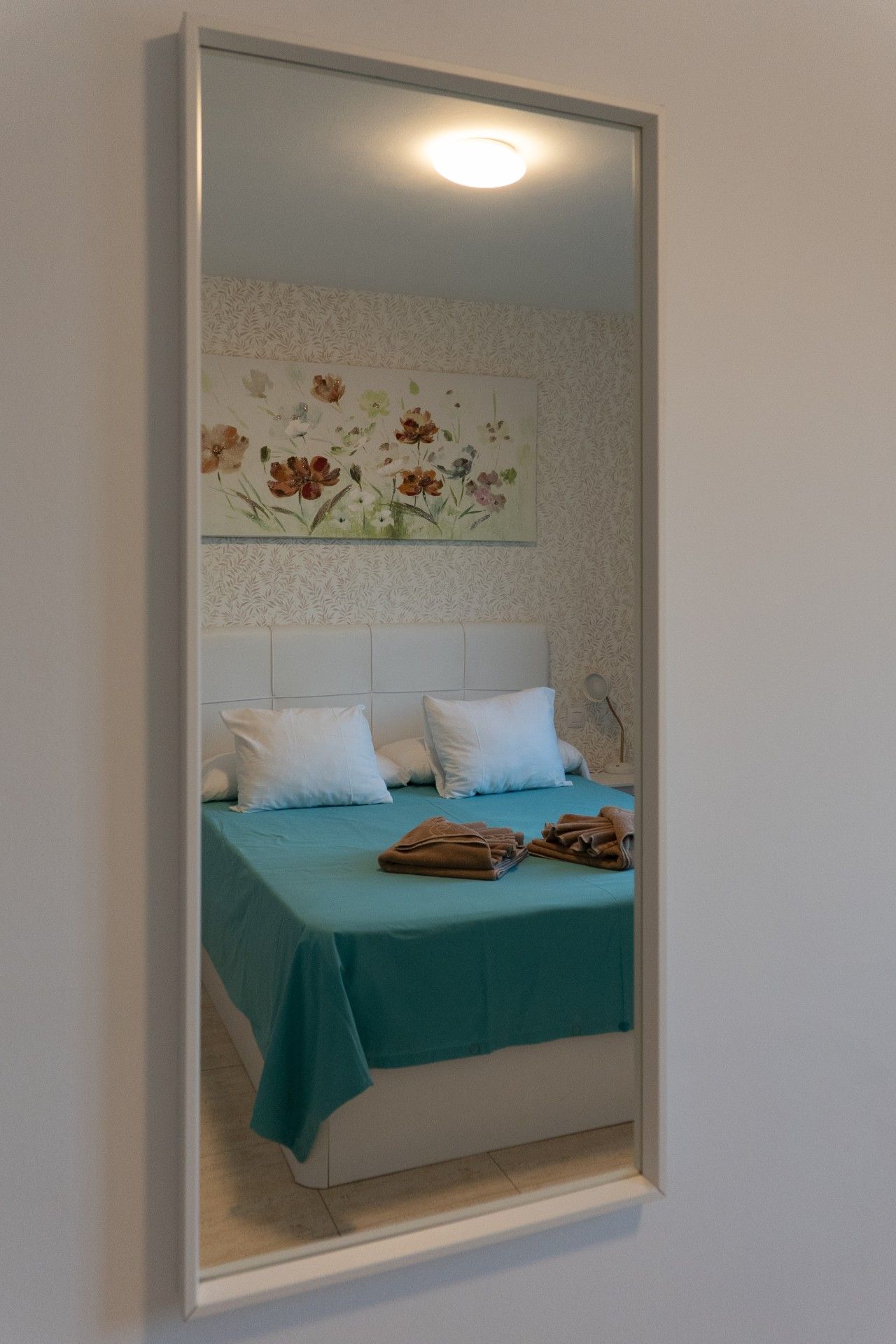 Quarto com cama, travesseiros, cobertor e espelho fixado na parede.
