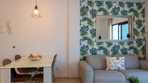 Ein Zimmer mit Esstisch, Stühlen, einer Couch, einem Spiegel und einer Pflanze auf einem Glastisch.