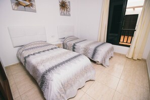 A bedroom with two beds, a white headboard, a small bedside table, and a window with curtains. - Sara 5, Playa Blanca (Playa Blanca)