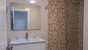 Ein Badezimmer mit einem weißen Waschbecken, einem Spiegel und einer Dusche mit Mosaikfliesen.