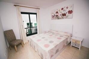 A bedroom with a bed, a chair, a nightstand, a painting, and a balcony view. - Sara 5, Playa Blanca (Playa Blanca)