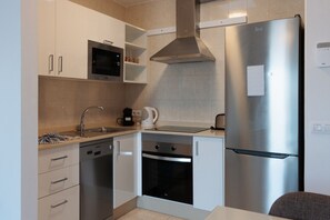 Eine kompakte Küche mit einem Edelstahl-Kühlschrank, einer Mikrowelle, einer Kaffeemaschine und einem Geschirrspüler.