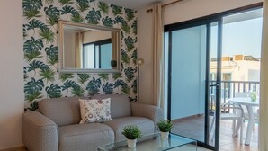 Ein Wohnzimmer mit einer Couch, einem Glastisch, einem Spiegel und einem Balkon mit Gartenmöbeln.