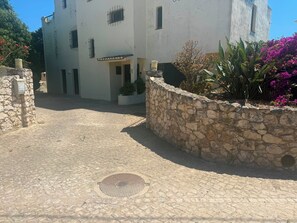 A stone-walled courtyard with a building entrance, a manhole cover, and a signboard. - SEAS THE DAY 2 (Luz)