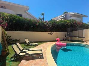 A swimming pool with lounge chairs, a pink flamingo float, and a white building with a green lawn. - SEAS THE DAY 2 (Luz)