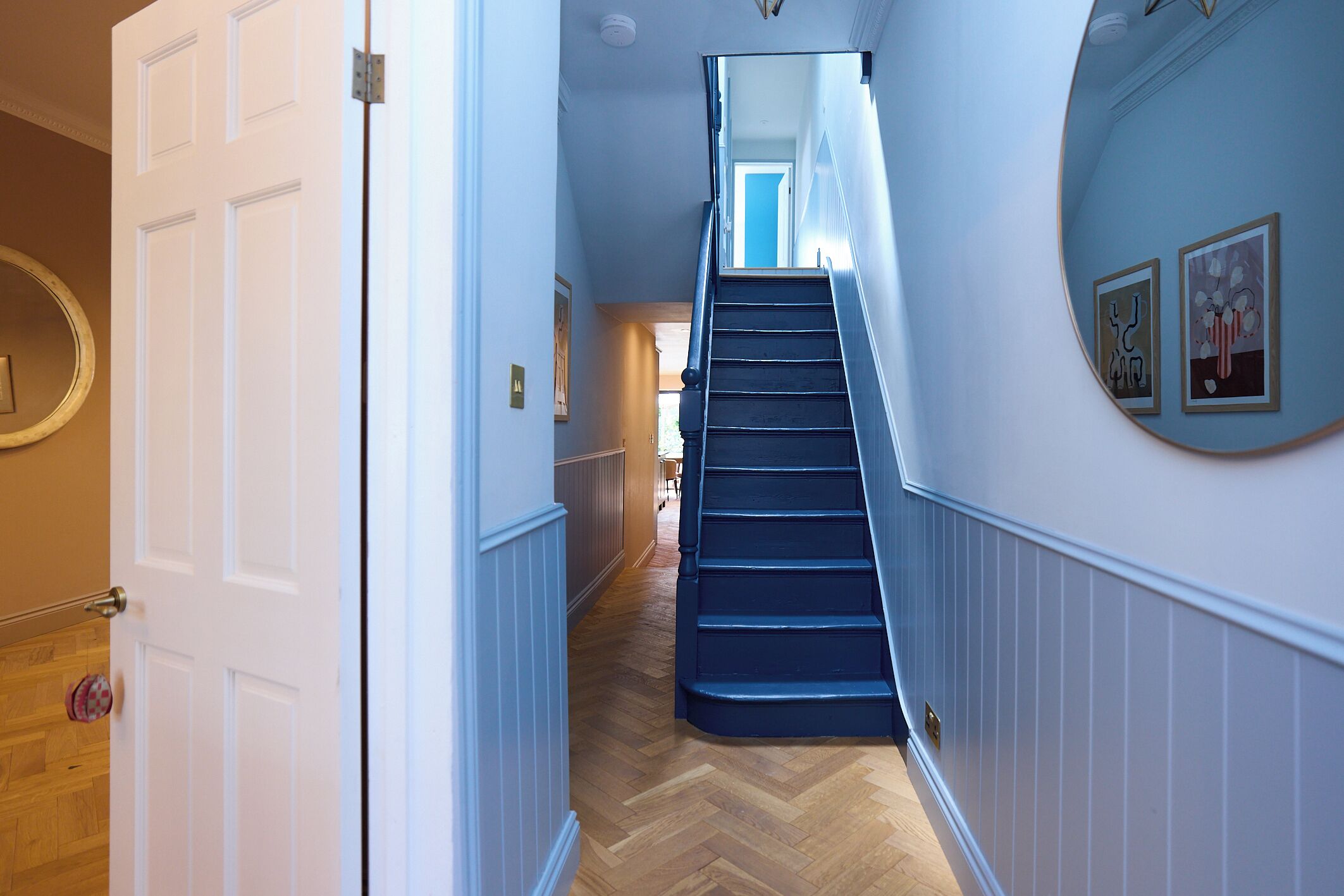 Un pasillo con piso de madera, una escalera azul y una puerta blanca.
