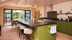 Cozinha moderna com uma ilha grande, armários verdes e iluminação pendente.