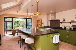 A modern kitchen with a large island, green cabinets, and pendant lighting. - The Cobalt & Olive Terrace - Peckham (London)