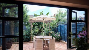 Um pátio com mesa e cadeiras, um toldo e vista para um jardim através de grandes janelas.