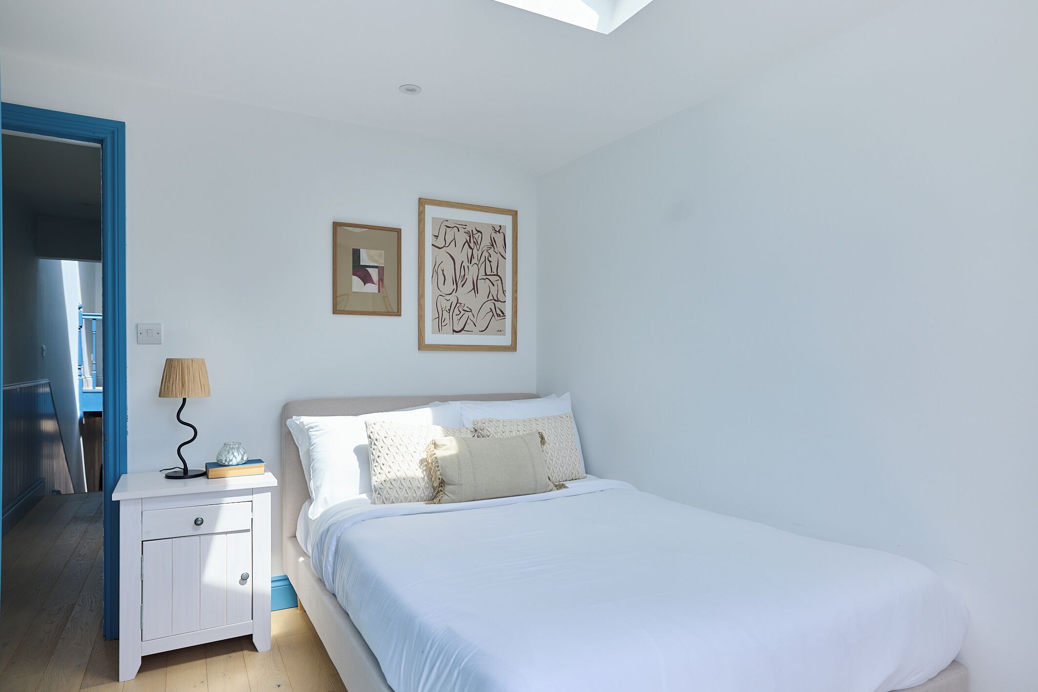 A bedroom with a bed, nightstand, lamp, and two framed artworks on the wall.