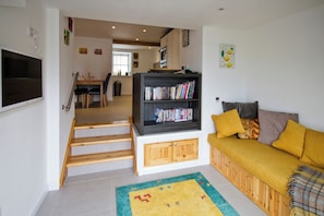 Una sala de estar con un sofá, una estantería, un televisor y una escalera que lleva a otra habitación.