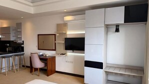 A hotel room with a bed, a desk, a chair, a television, a wardrobe, and a kitchenette.