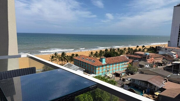 A balcony with a view of the beach, palm trees, and buildings.