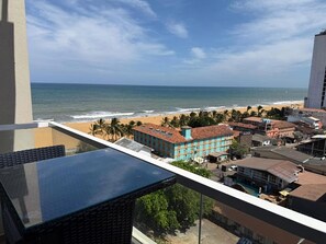 Un balcón con vistas a la playa, palmeras y edificios.