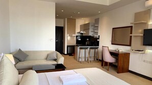 A hotel room with a bed, a sofa, a desk, a chair, and a kitchenette.