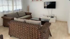 Een woonkamer met rieten meubels, een flatscreen televisie en een witte kast.