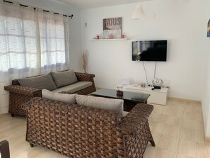 A living room with wicker furniture, a flat-screen TV, and a white cabinet. - Villa Rubicón Costa, Playa Blanca (Playa Blanca)
