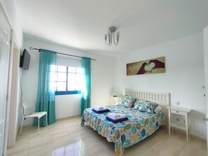 A bedroom with a bed, a chair, a TV, a painting, and a window with curtains. - Villa Rubicón Costa, Playa Blanca (Playa Blanca)
