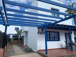 A building with a blue roof structure, a sign reading 'Villa Rubicon Costa,' and a patio area with chairs and a table. - Villa Rubicón Costa, Playa Blanca (Playa Blanca)