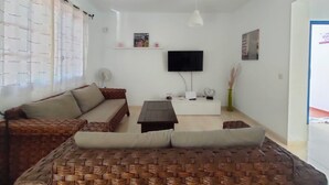 Een woonkamer met een bank, een salontafel, een flatscreen-tv en een wit kastje.
