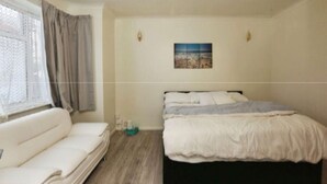 Een slaapkamer met een bed, een slaapbank, een raam met gordijnen en een aan de muur hangend schilderij.
