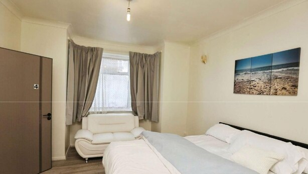 Een slaapkamer met een bed, een stoel, een kledingkast, een raam met gordijnen en een schilderij aan de muur.