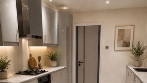 Een moderne keuken met een kookplaat, oven en wasmachine, een eethoek met een tafel en stoelen, en een deur die leidt naar een andere kamer.
