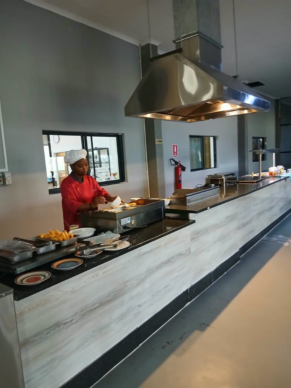 A chef preparing food in a modern kitchen with a large stainless steel hood and a marble countertop.