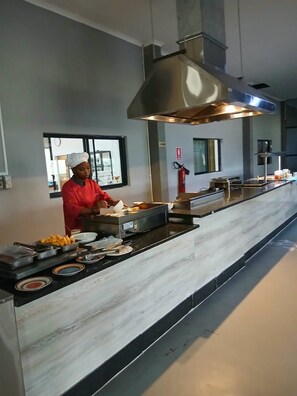 A chef preparing food in a modern kitchen with a large stainless steel hood and a marble countertop. - GreenLand Hotel (Kasane)