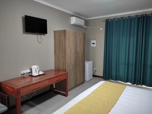 A hotel room with a bed, a wooden desk, a television, an air conditioner, and a curtain. - GreenLand Hotel (Kasane)