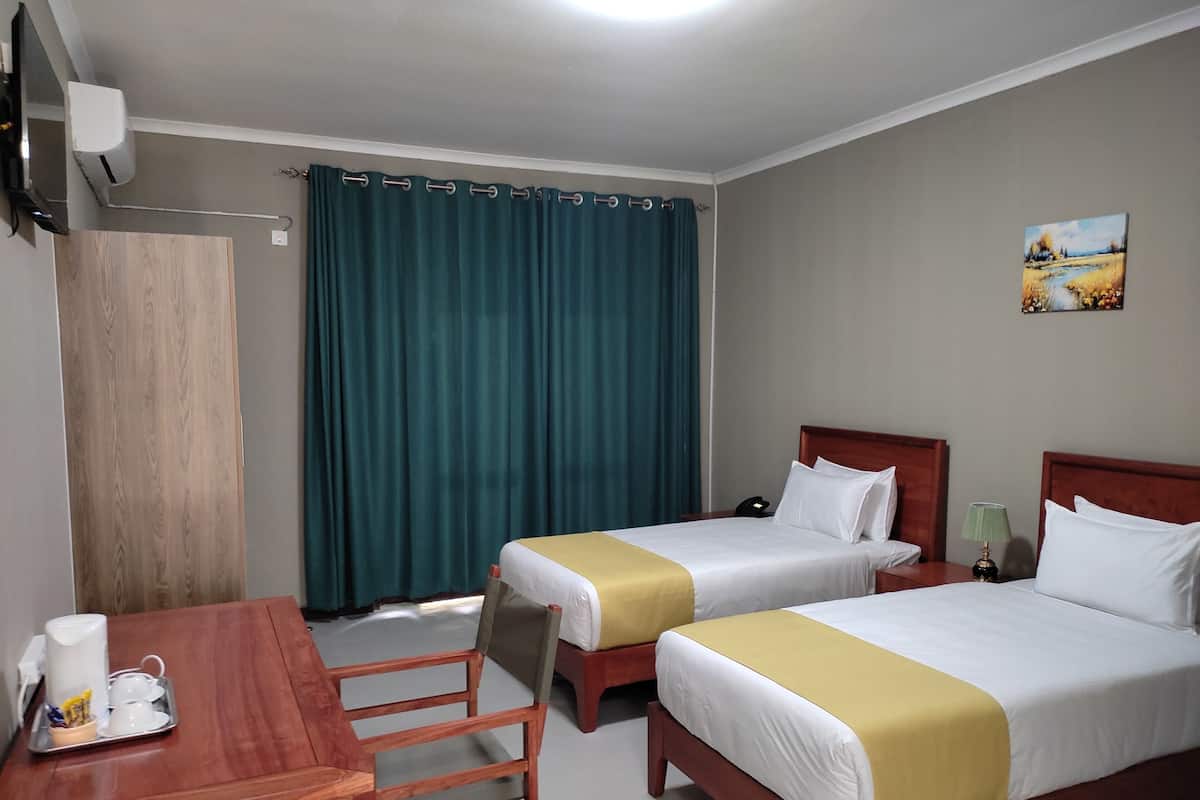 A hotel room with two beds, a desk, a chair, a painting on the wall, and a window with curtains.