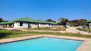 A pool area with a rectangular pool, a building with a green roof, and a clear blue sky.