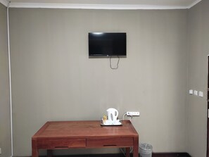 A room with a wooden table, a television mounted on the wall, and a power outlet. - GreenLand Hotel (Kasane)