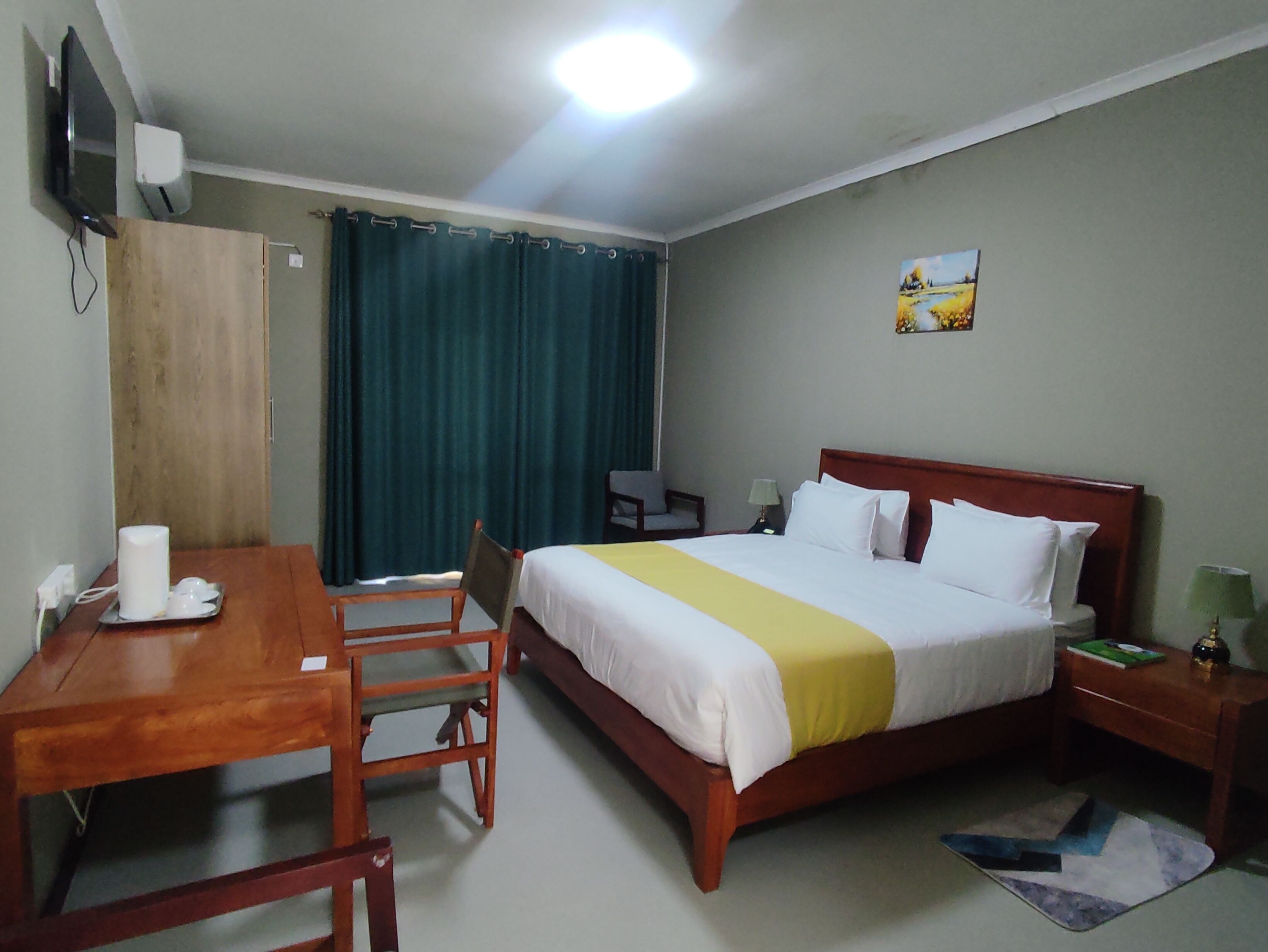 Hotelkamer met een bed, bureau, stoel, televisie en schilderij aan de muur.