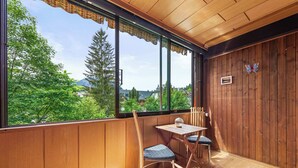 A room with wooden walls, a large window with a view of greenery and buildings, a table with chairs, and a decorative butterfly on the wall. - Riverview Apartment | Kitchen | Parking | Loggia (Bad Aussee)