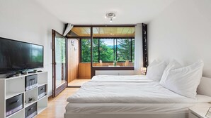 A bedroom with a large bed, a TV, and a view of greenery through a sliding door. - Riverview Apartment | Kitchen | Parking | Loggia (Bad Aussee)