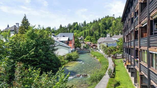 A riverside view with buildings, a bridge, and a well-maintained garden. - Riverview Apartment | Kitchen | Parking | Loggia (Bad Aussee)