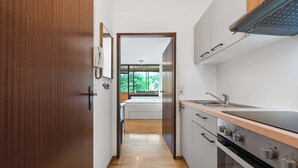 A narrow kitchen with a wooden door, a view into a bedroom, and a modern stove. - Riverview Apartment | Kitchen | Parking | Loggia (Bad Aussee)