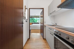 Una cocina estrecha con puerta de madera, vista a un dormitorio y estufa moderna.